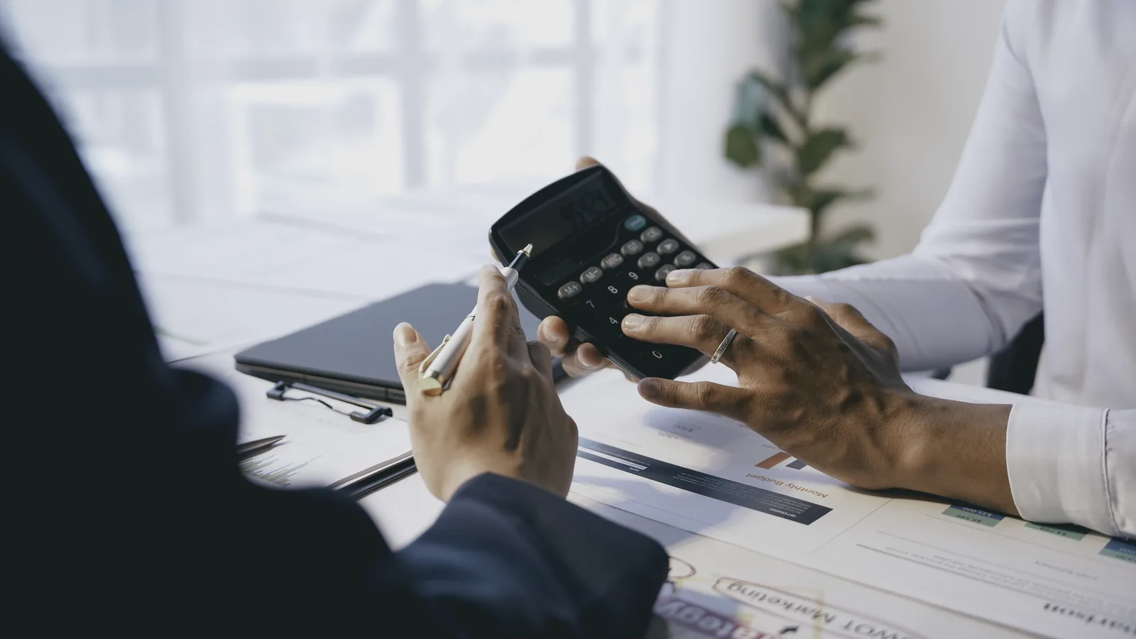 Two people at a desk, one holding a calculator over paperwork.