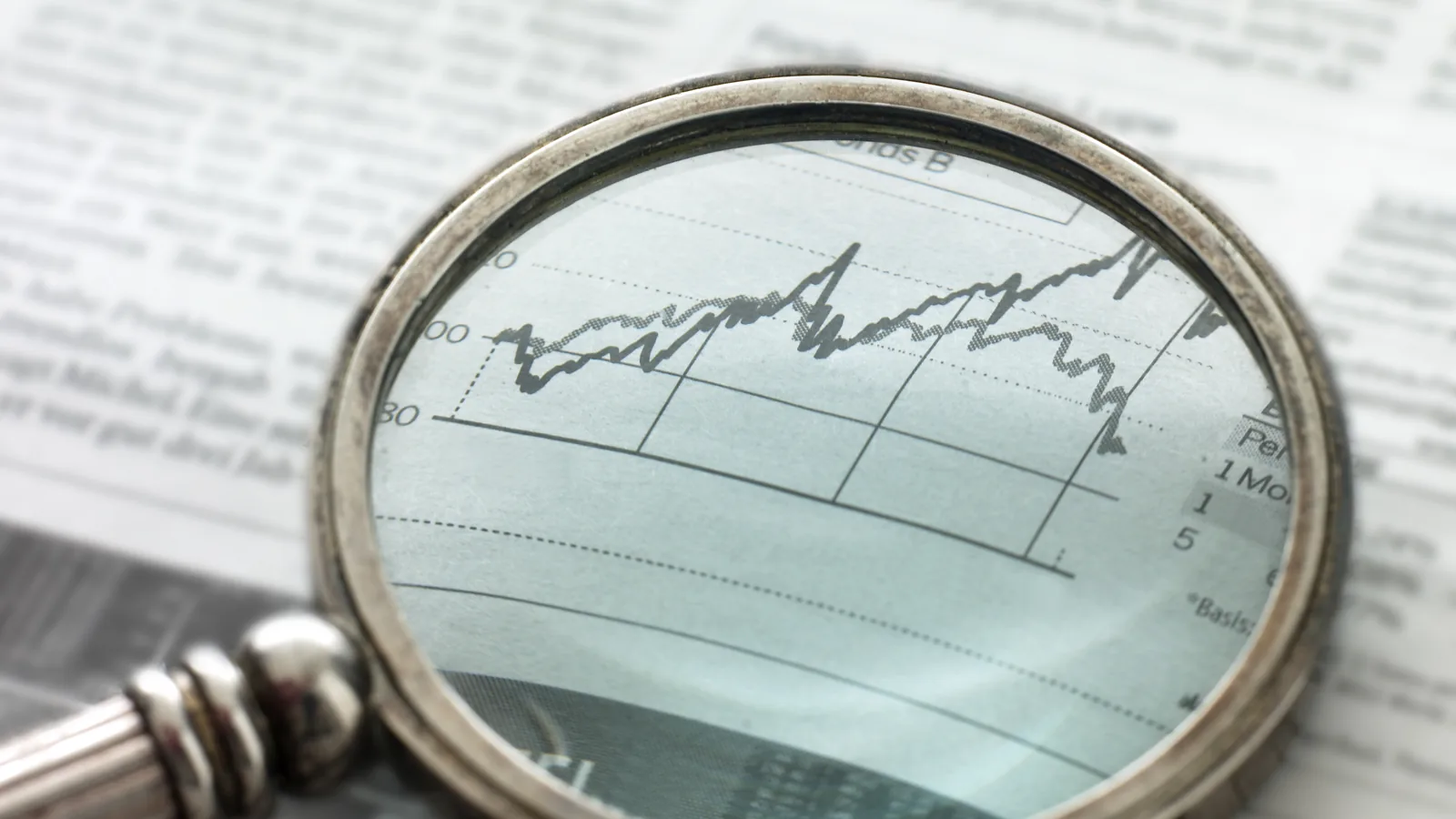 A magnifying glass resting on a newspaper, enlarging a printed market chart.