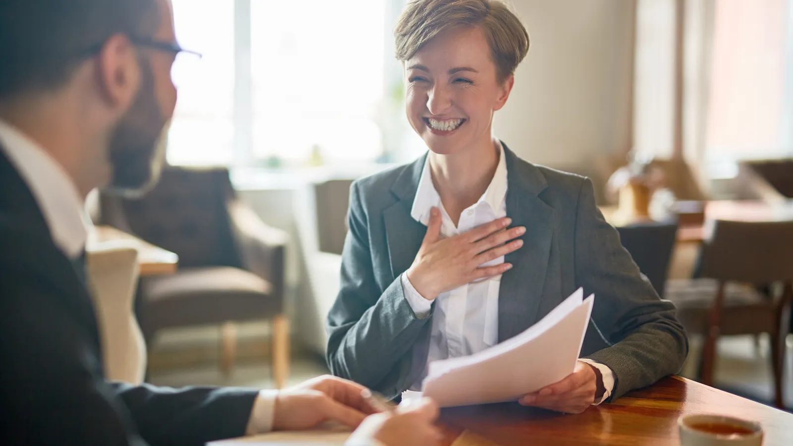 Two people in a meeting across a table, one holding a document.