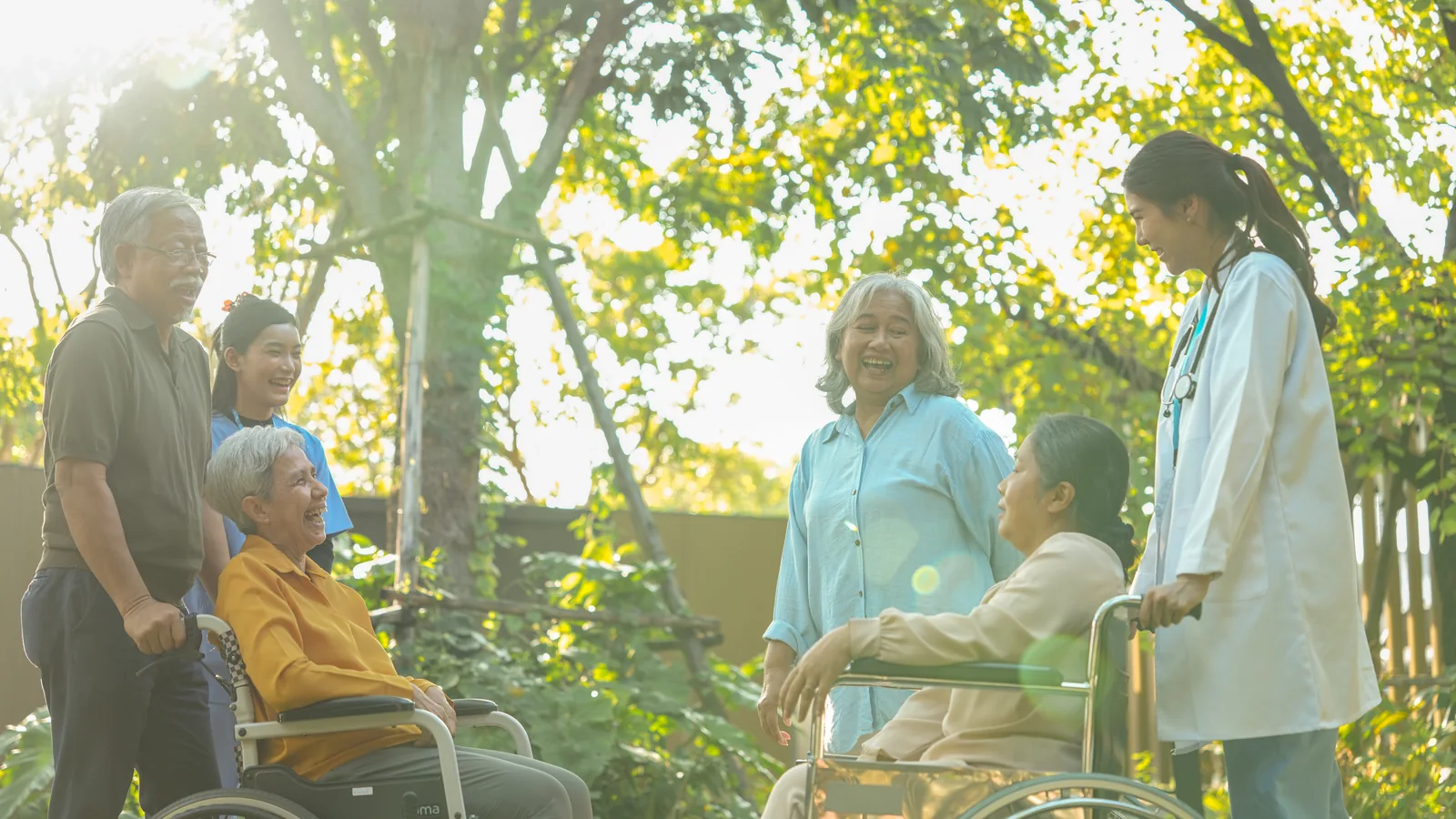Caregivers walking outdoors with older adults in wheelchairs.