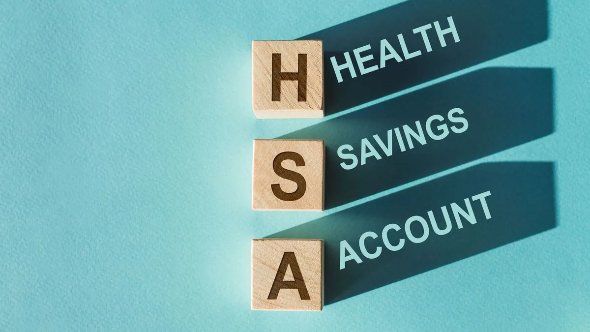 Wooden letter tiles spelling HSA on a teal background, their shadows reading health savings account.