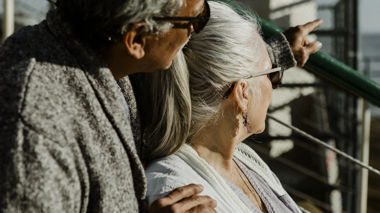 An older couple looking out from a railing, one of them pointing into the distance.