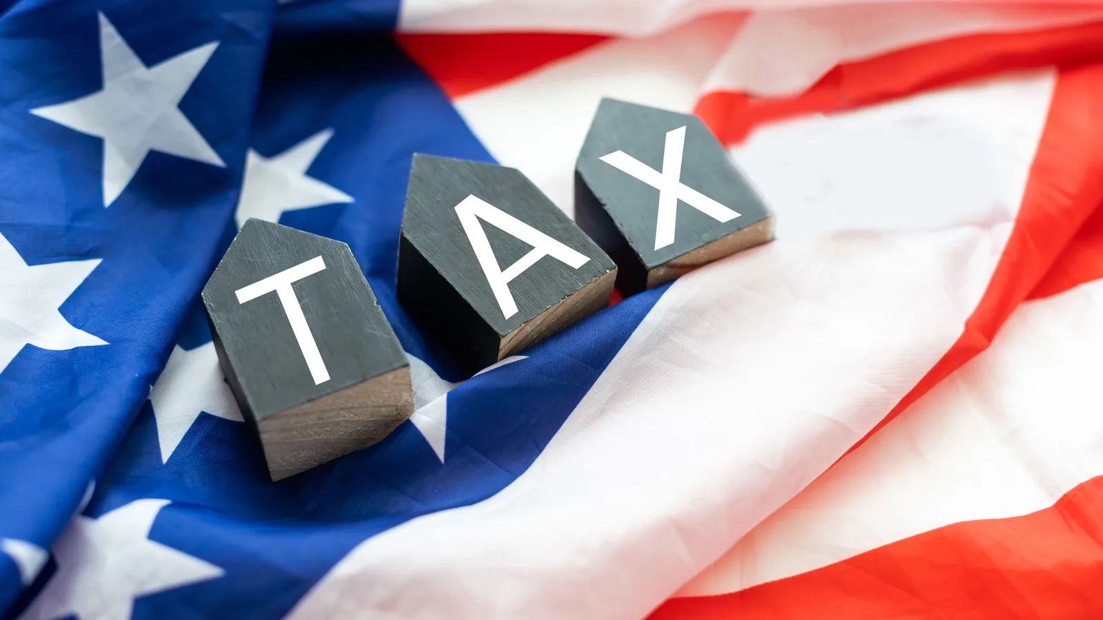 Wooden tiles spelling TAX resting on an American flag.
