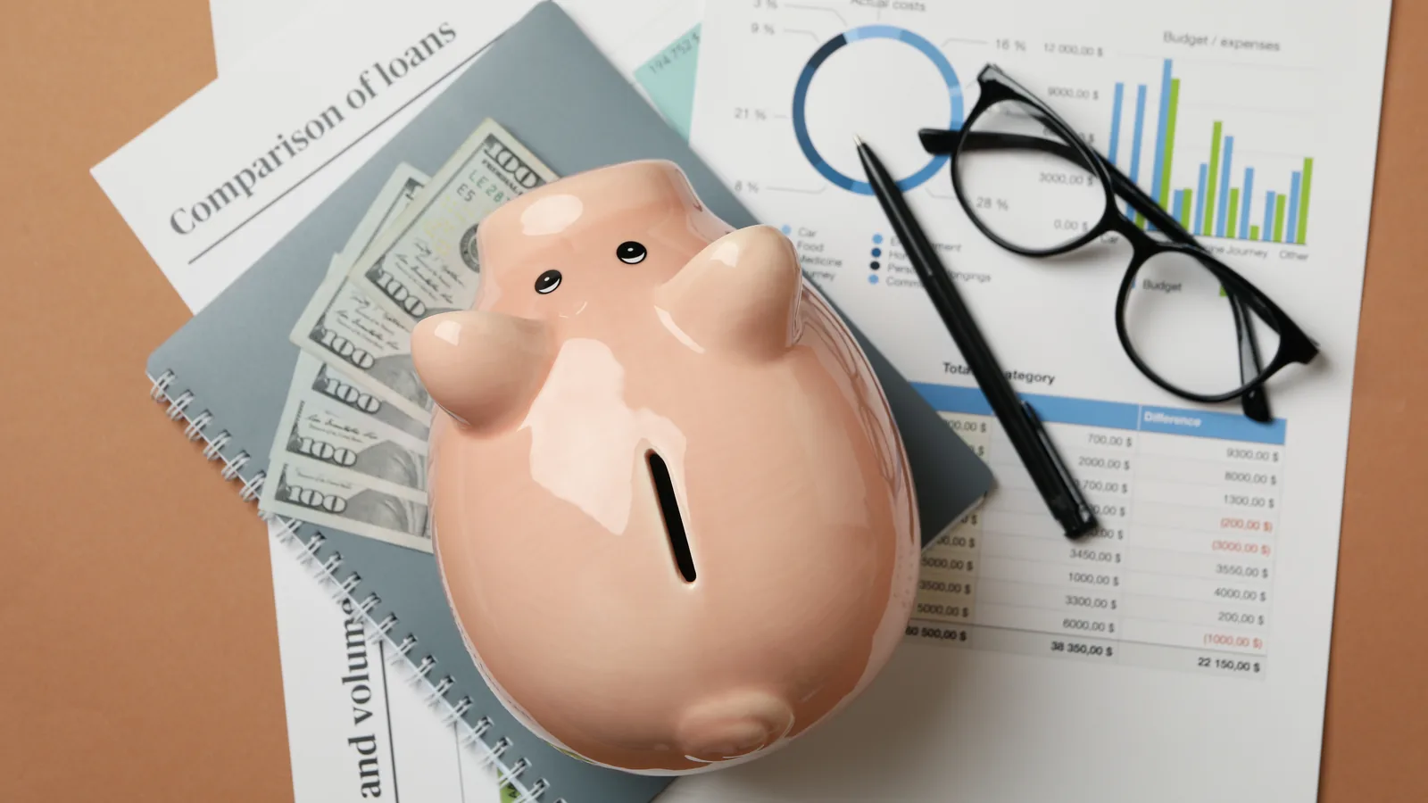 A piggy bank resting on printed charts, loan comparisons, and banknotes.